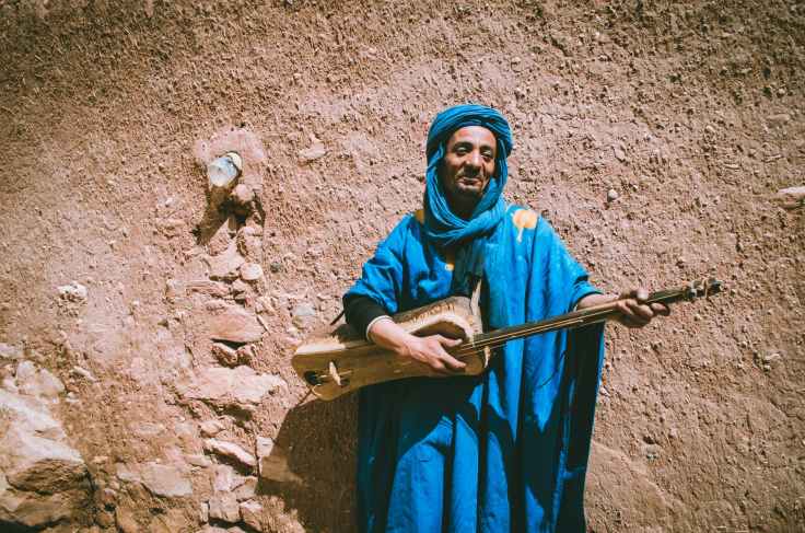 man wearing blue top holding brown string instrument